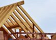 Partially built wooden house frame with exposed beams under a clear sky.